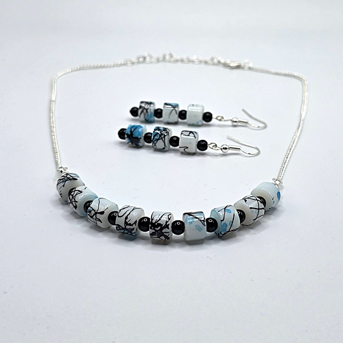 Necklace and earrings set with black and blue painted white beads on a light gray background