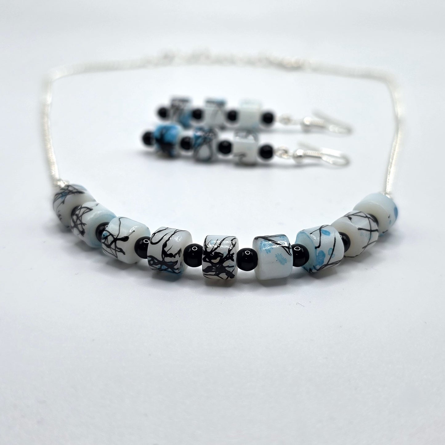 Beaded necklace and earrings with black, white, and blue pattern on a white background
