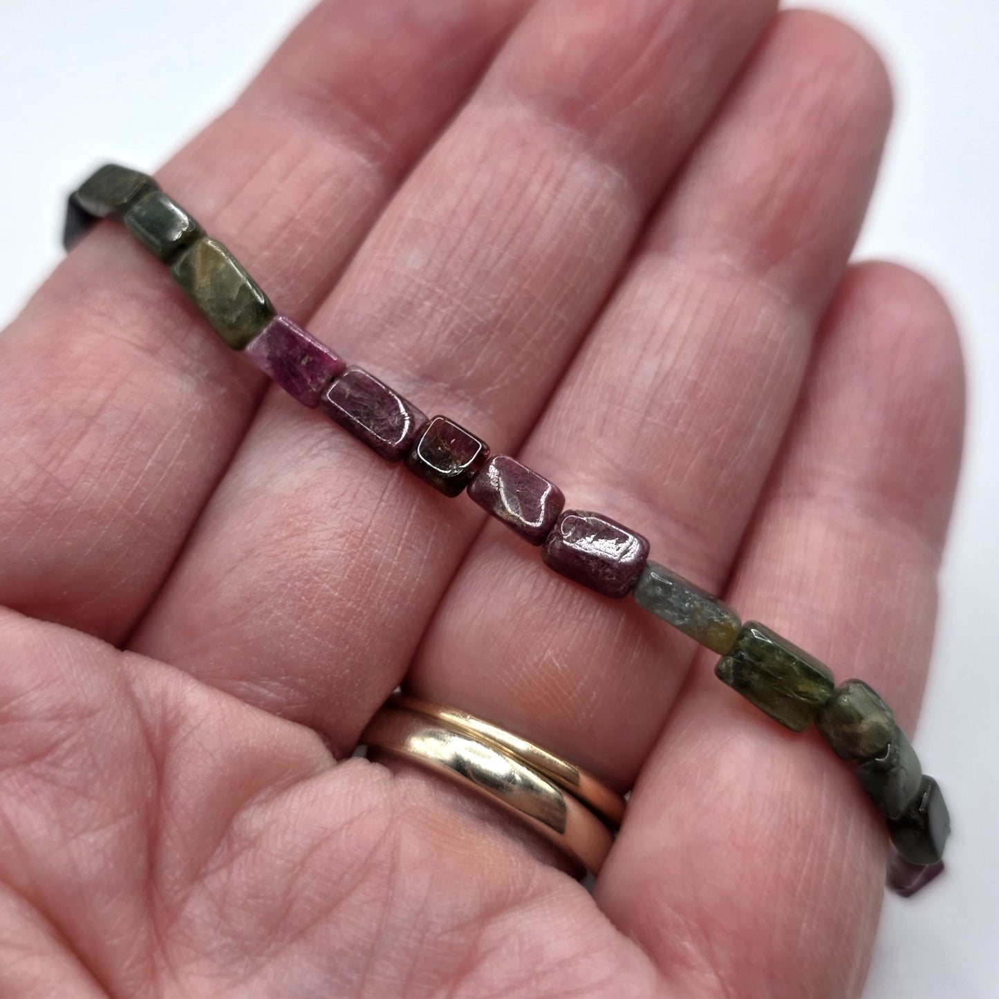 Hand holding a necklace with pink and green tourmaline beads on a white background