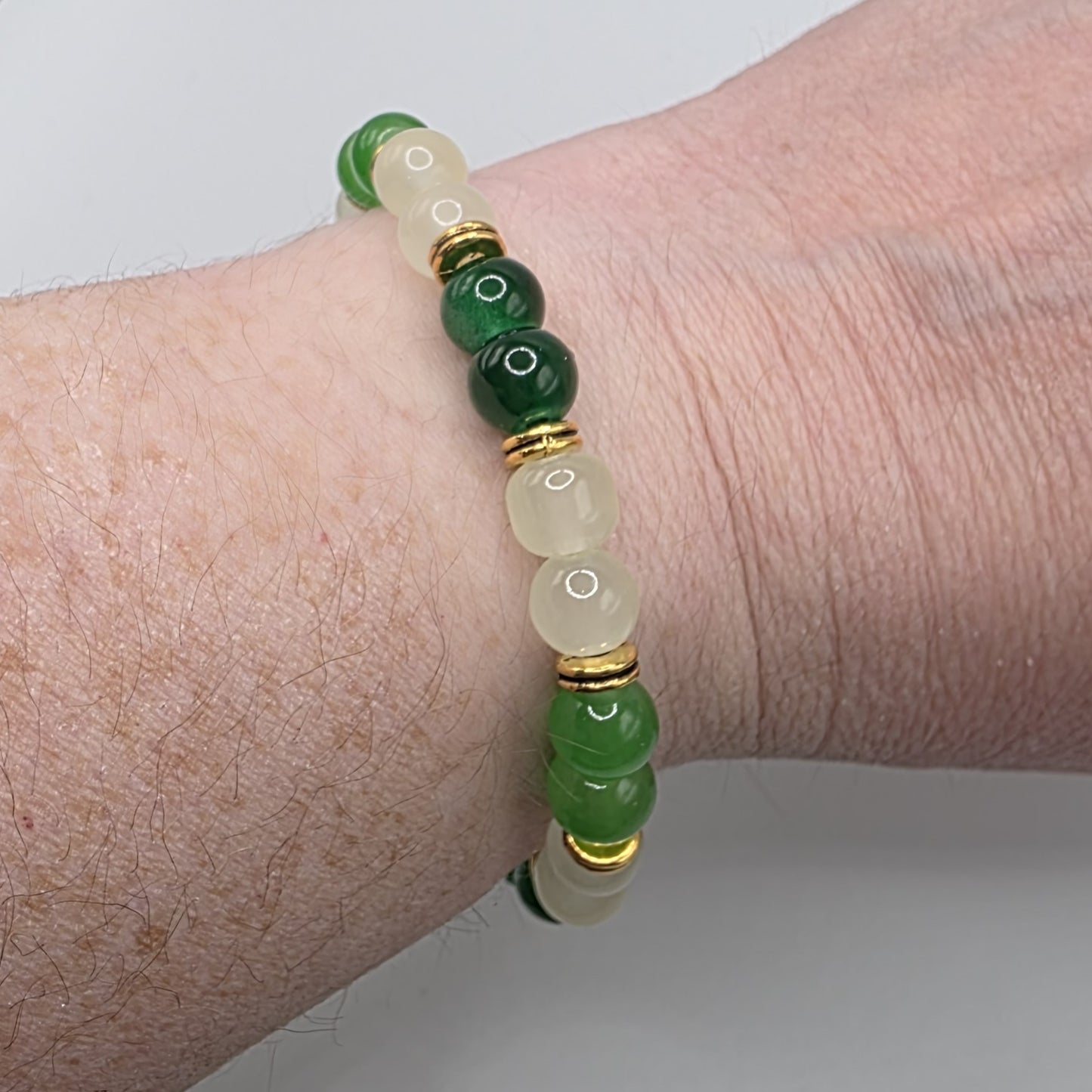 Green and gold beaded bracelet on a wrist against a neutral background