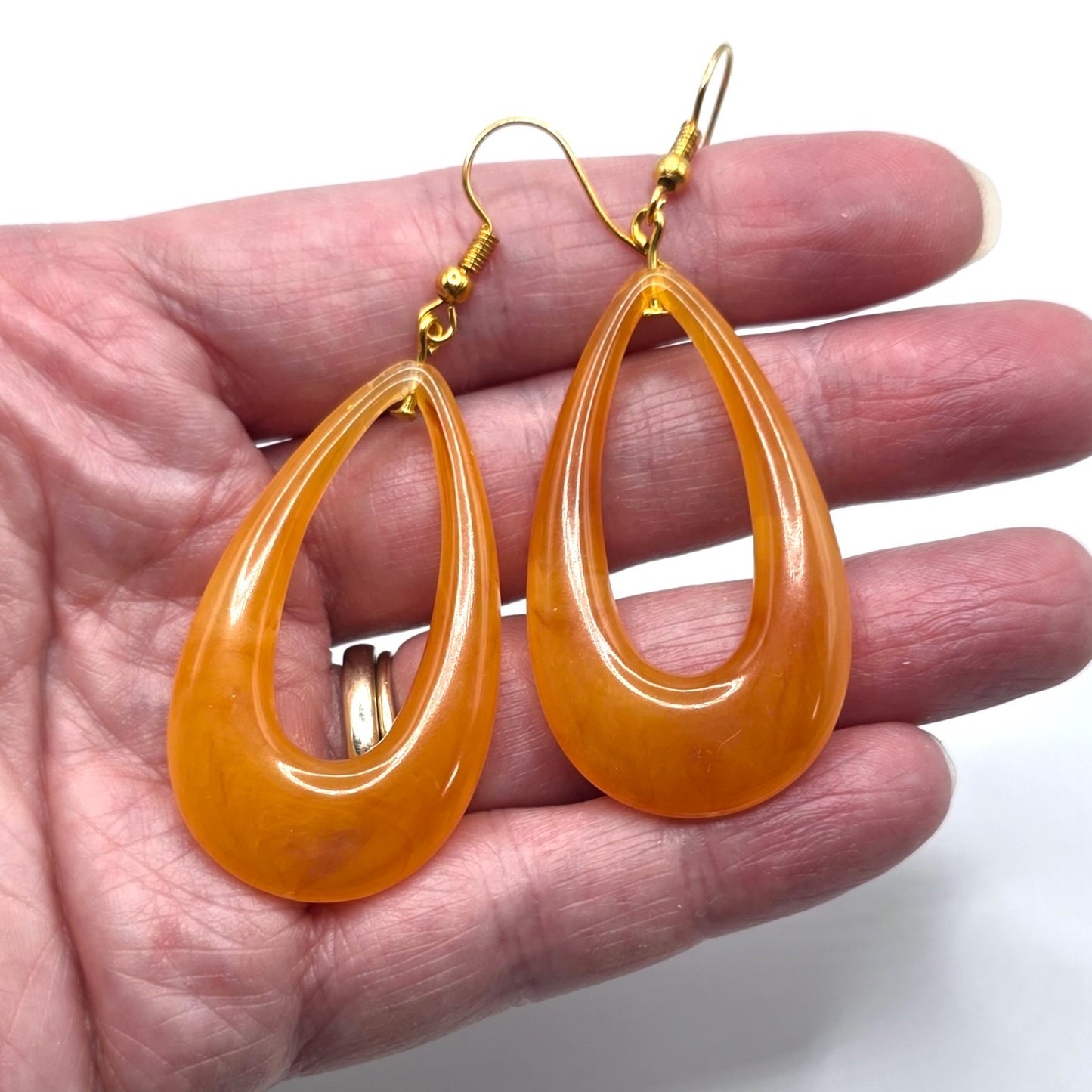 Orange teardrop earrings held in a hand against a white background