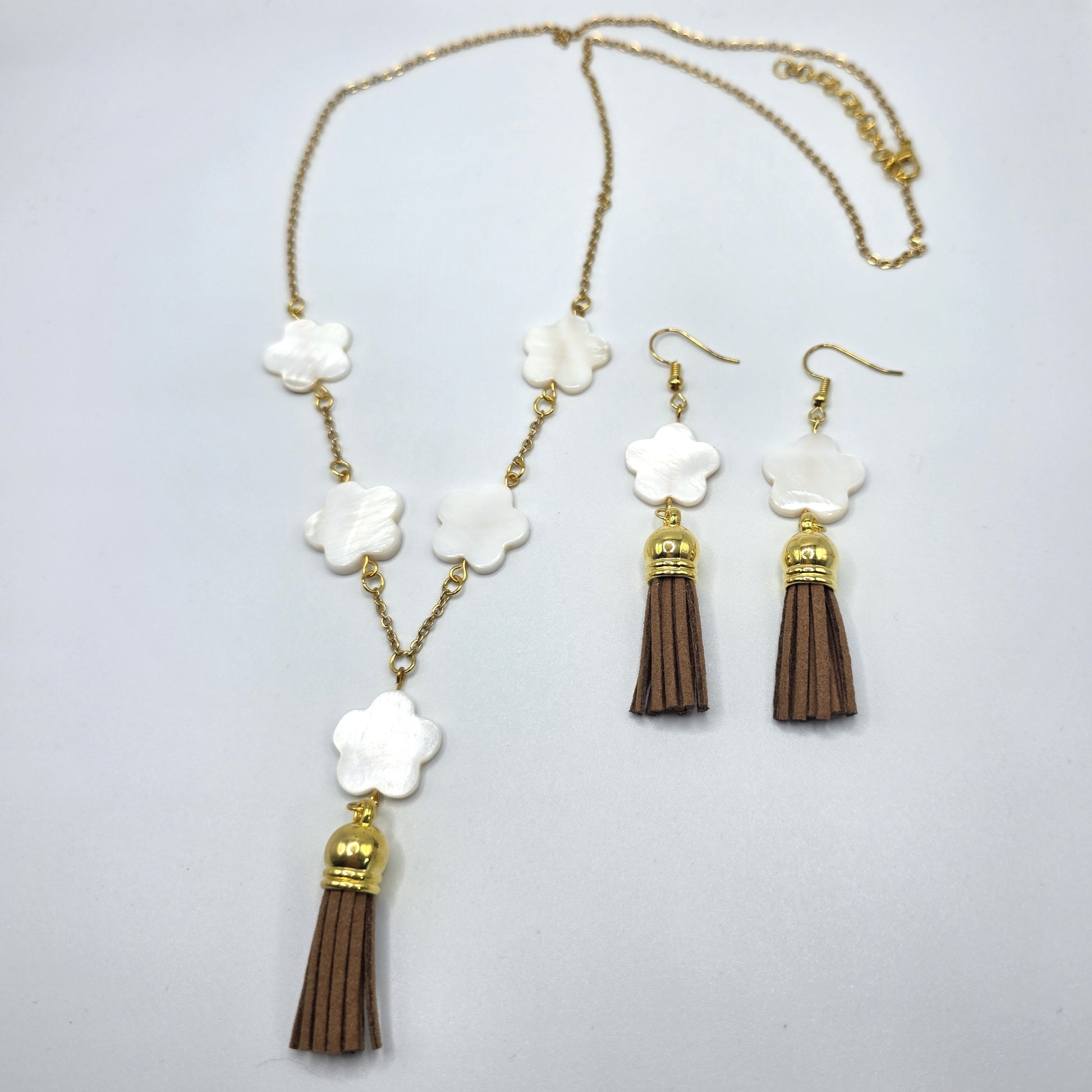 Jewelry set with necklace and earrings featuring white floral elements and brown tassels on a light gray background.
