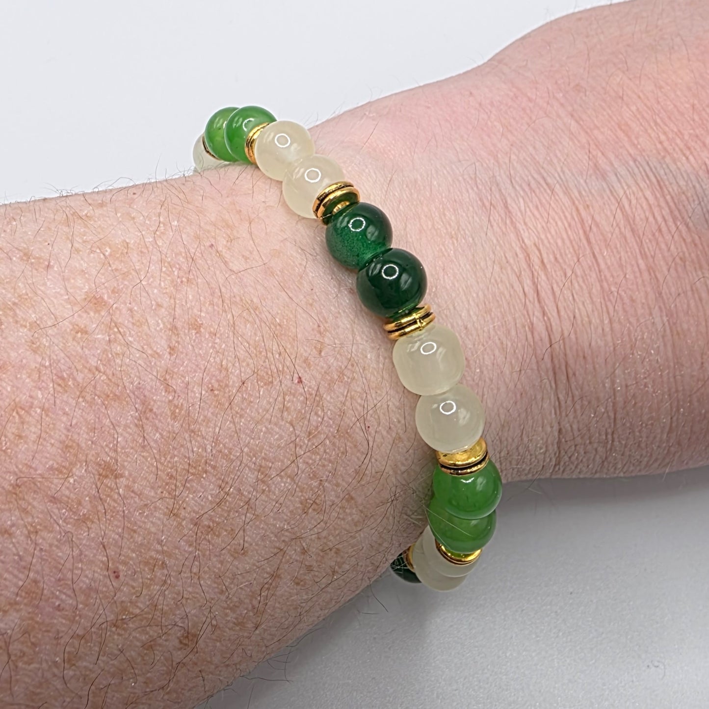 Green and gold beaded bracelet on a wrist against a light background