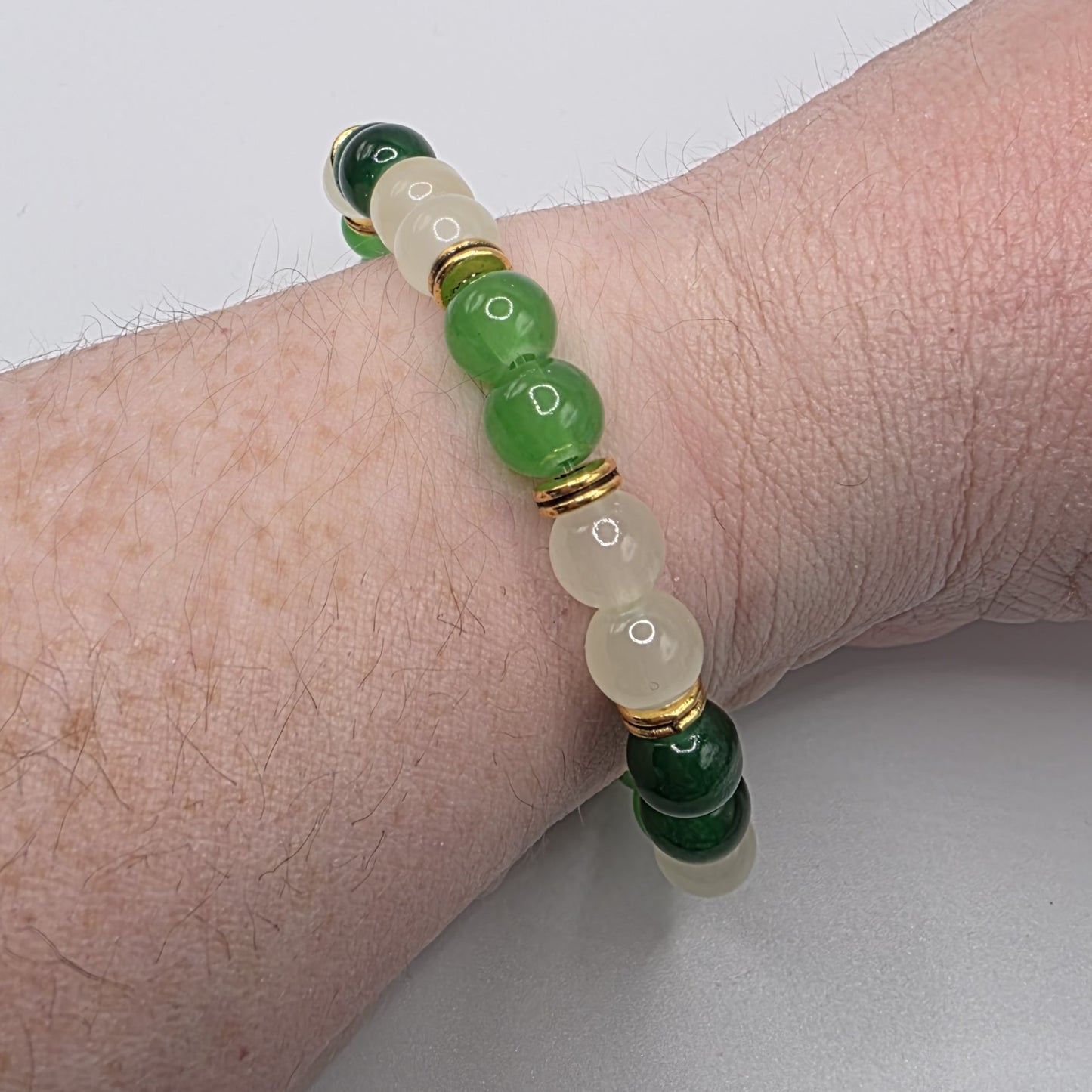 Bracelet with green and gold beads on a wrist against a white background
