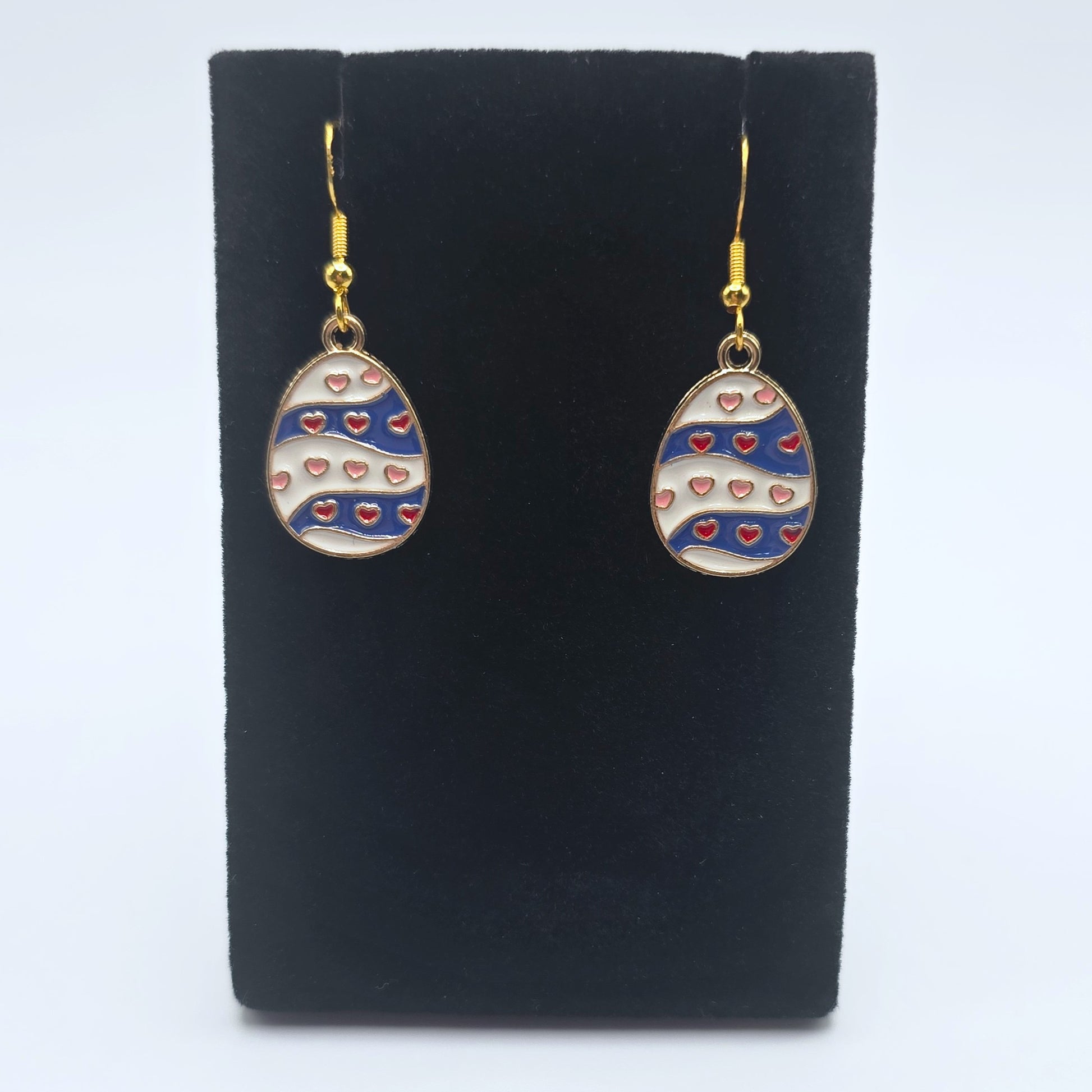 Easter egg-shaped earrings with heart patterns on a black stand against a white background