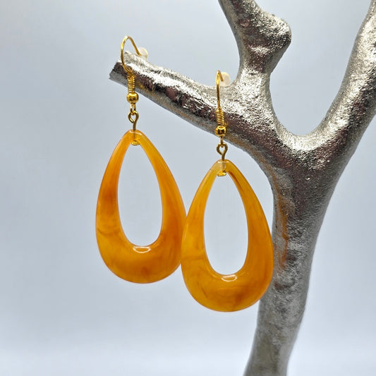 Pair of orange teardrop earrings on a silver branch against a light gray background