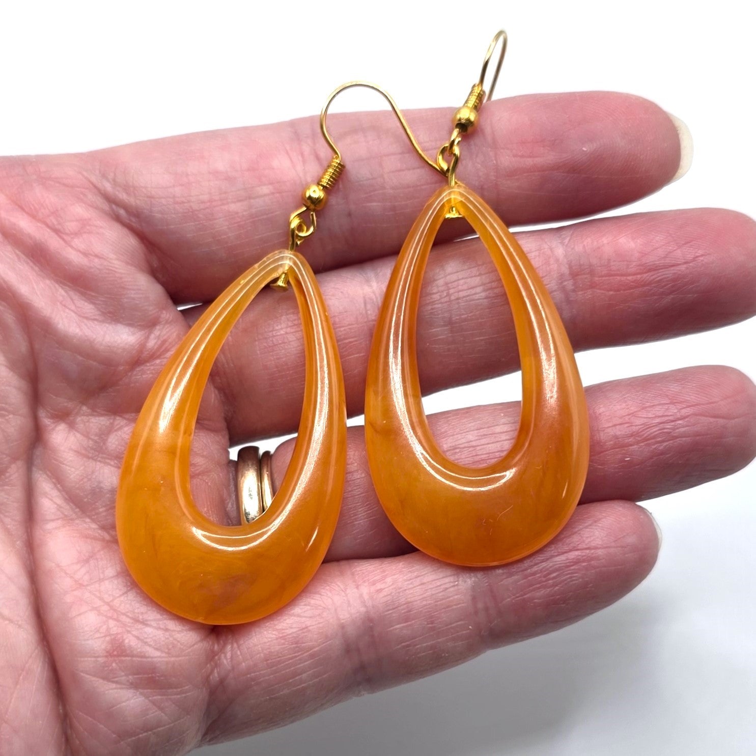 Orange teardrop earrings held in a hand against a white background