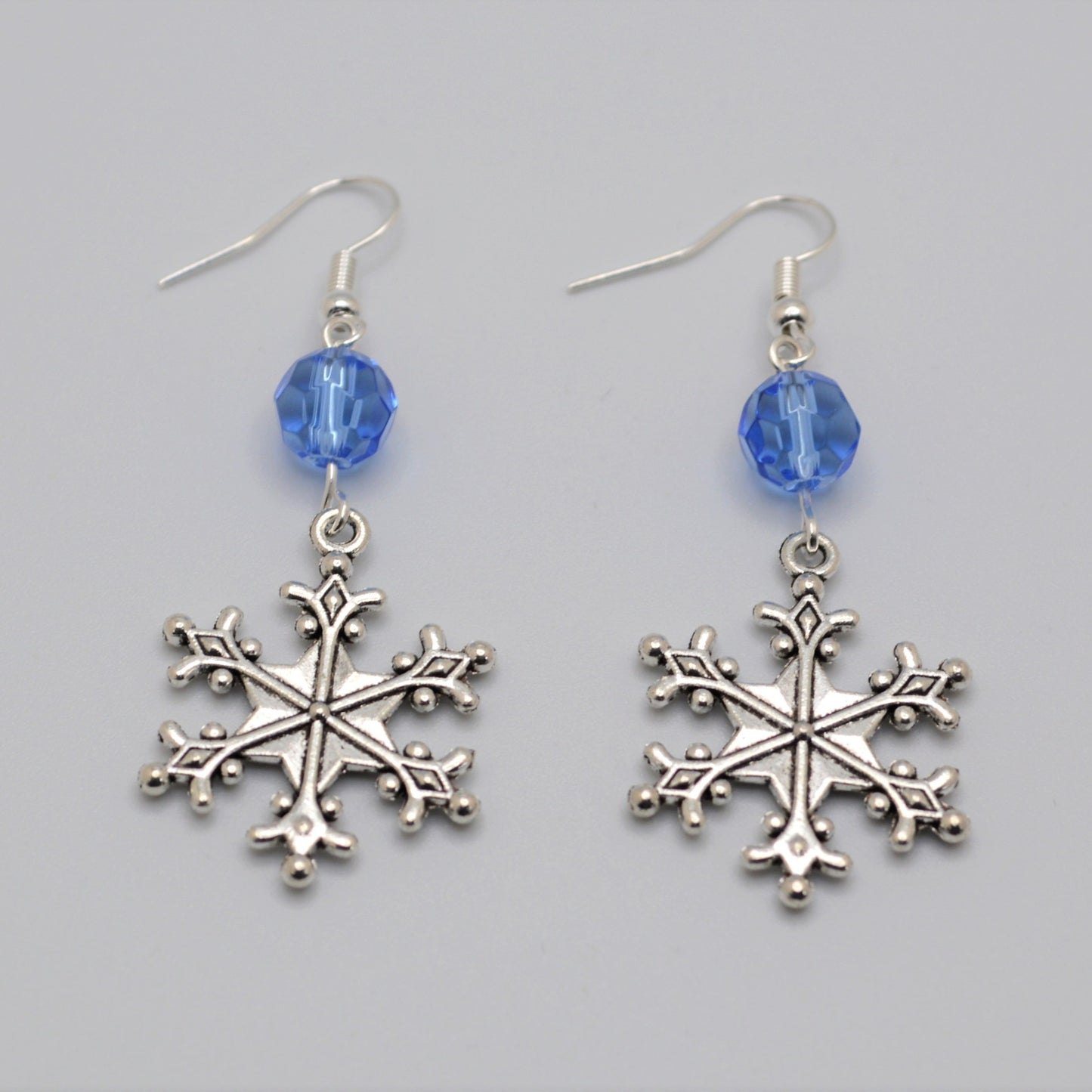 Silver snowflake earrings with blue beads on a gray background