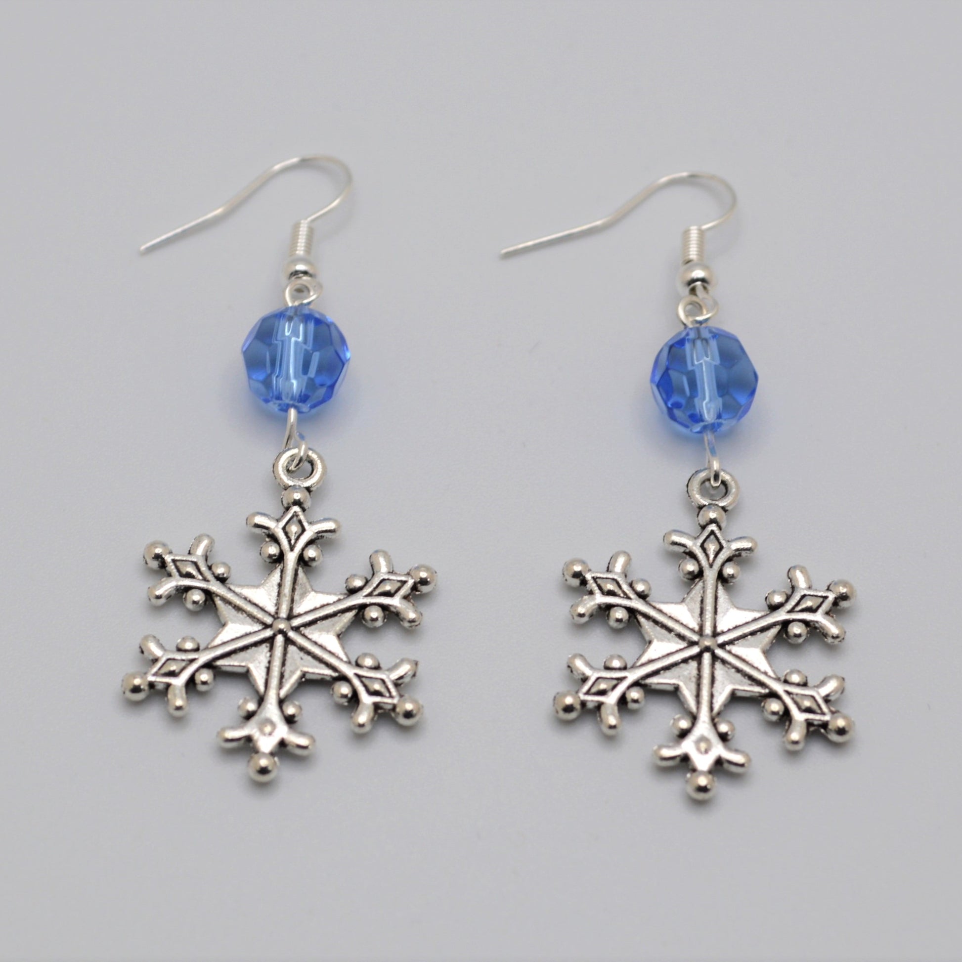 Silver snowflake earrings with blue beads on a gray background