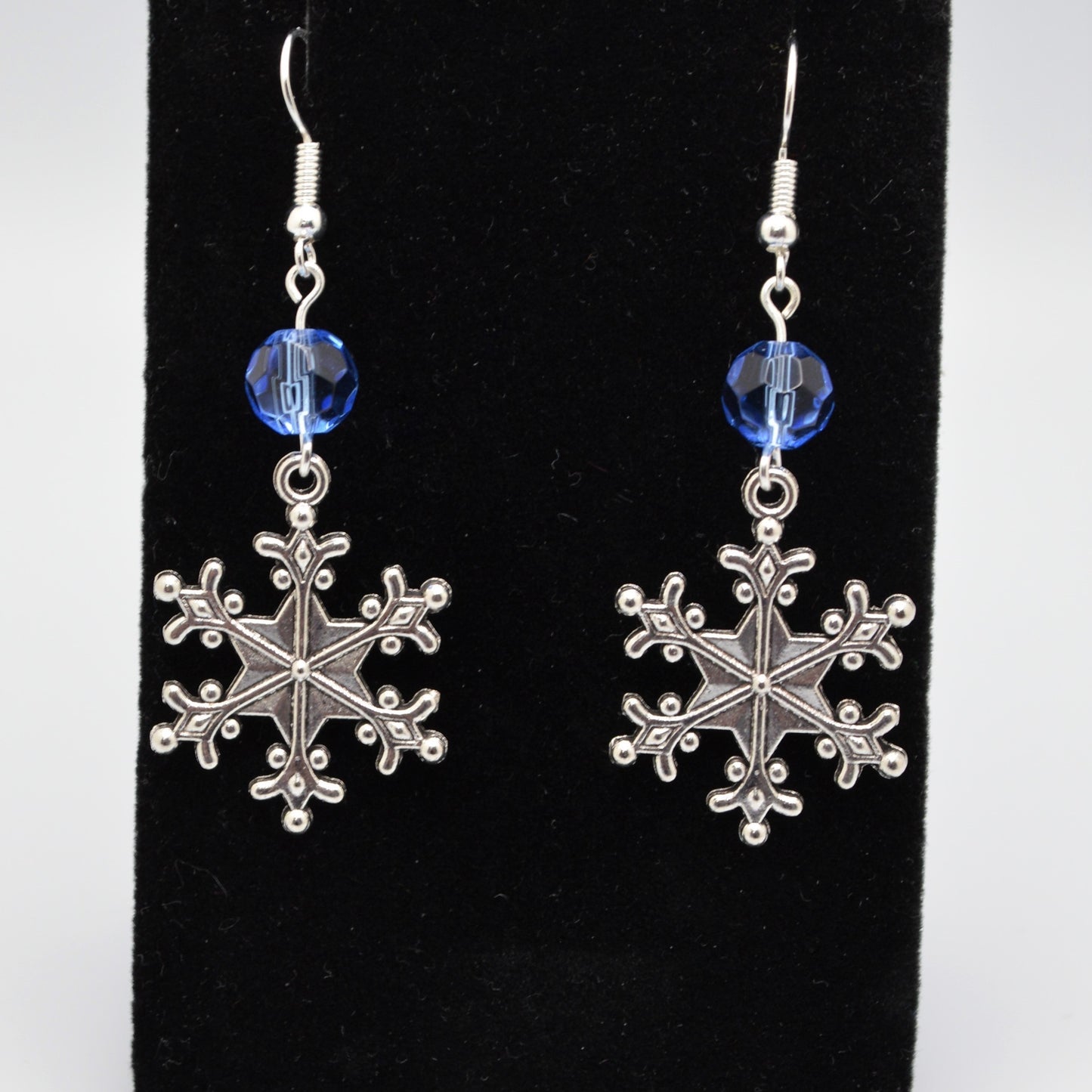 Silver snowflake earrings with blue beads on a black background