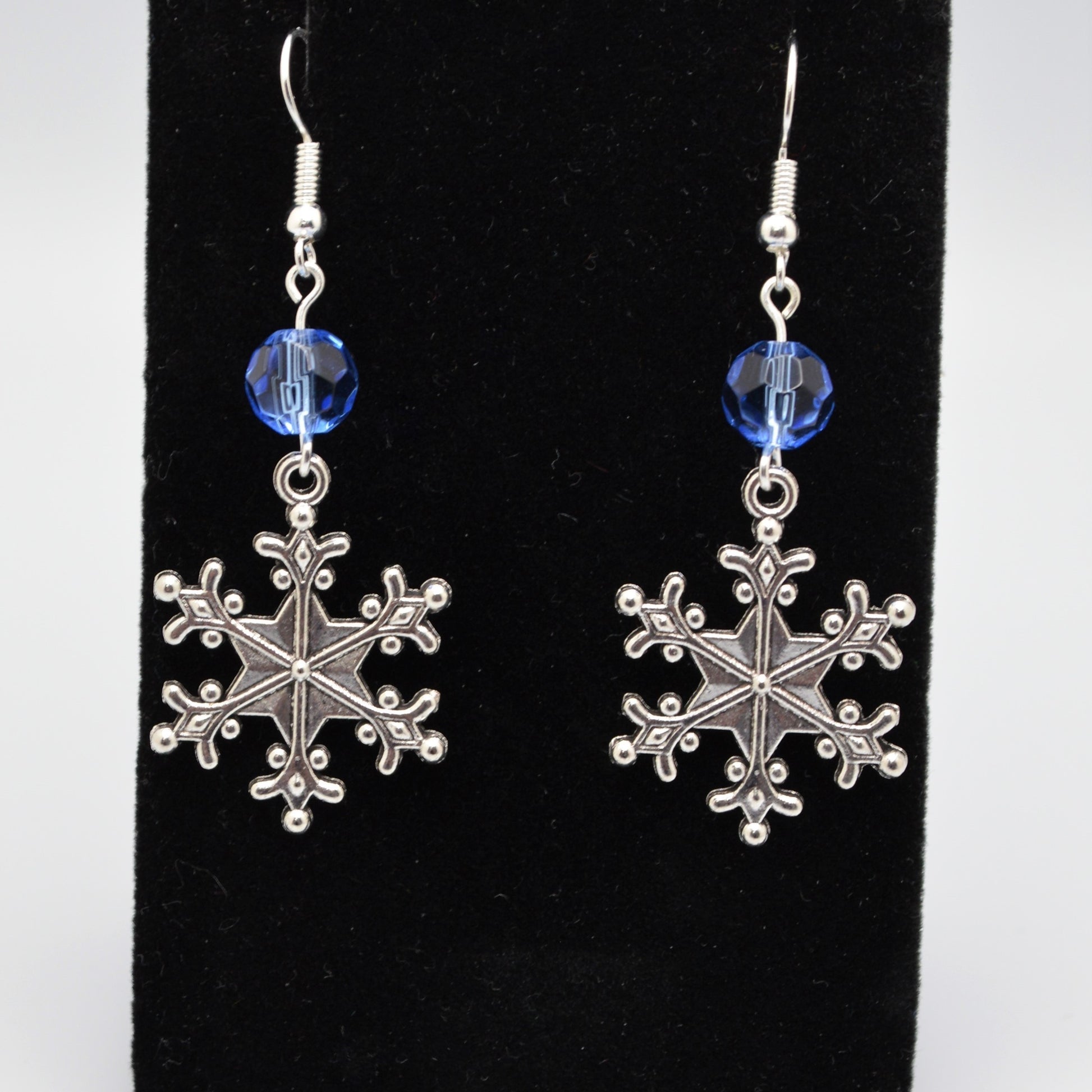 Silver snowflake earrings with blue beads on a black background