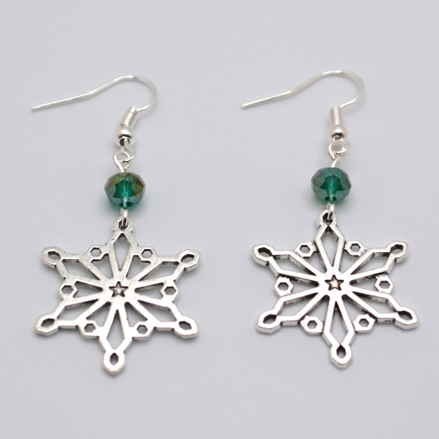 Silver snowflake earrings with green beads on a gray background