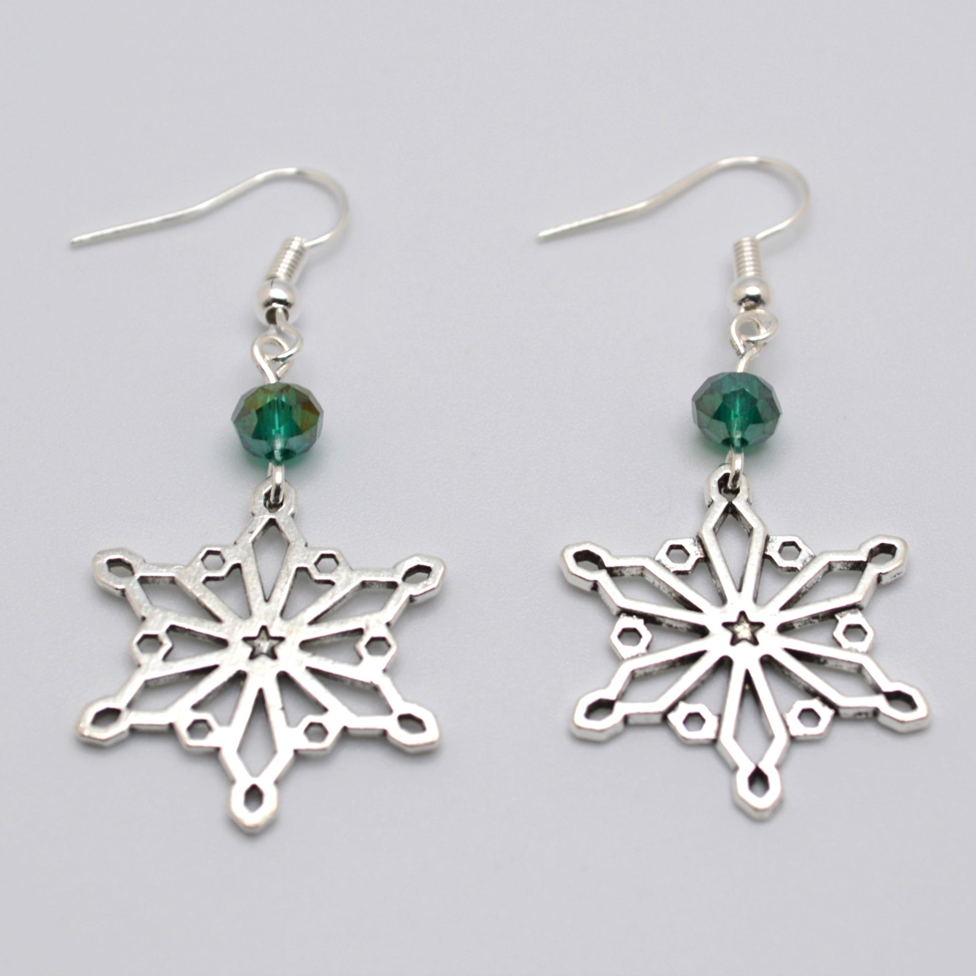 Silver snowflake earrings with green beads on a gray background