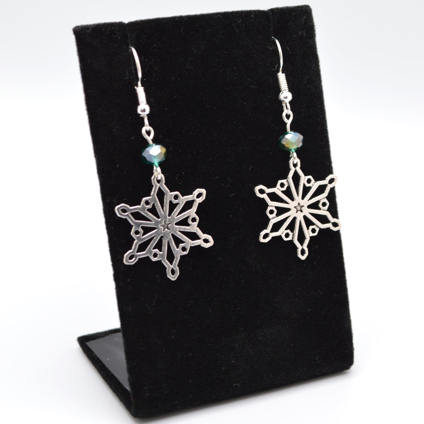 Silver snowflake earrings on a black display stand with a white background