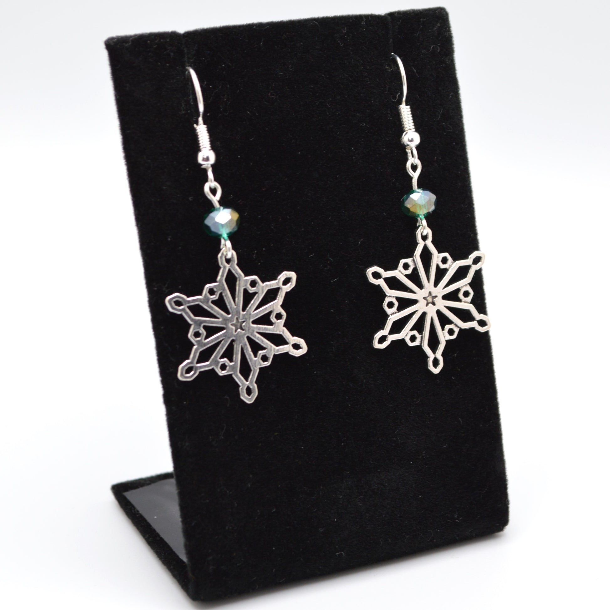 Silver snowflake earrings on a black display stand with a white background