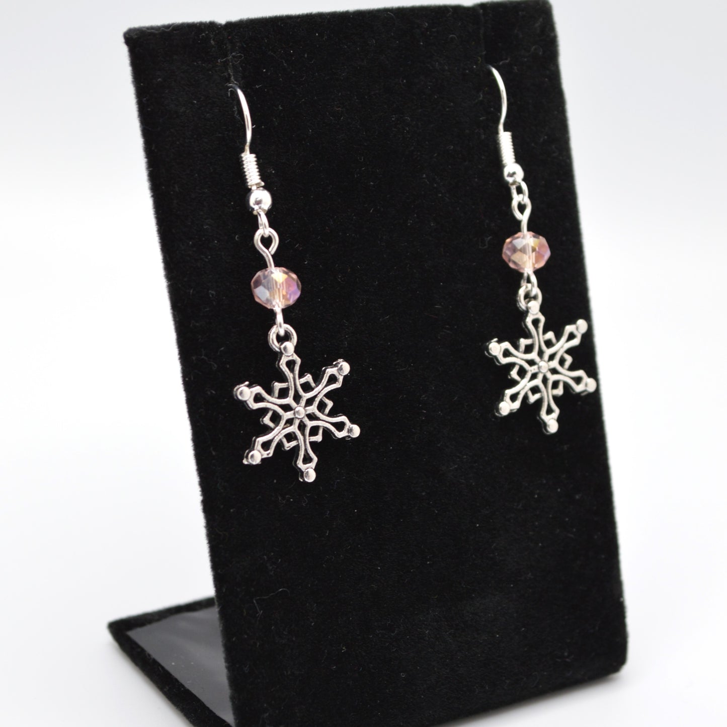 Silver snowflake earrings with pink beads on a black stand.