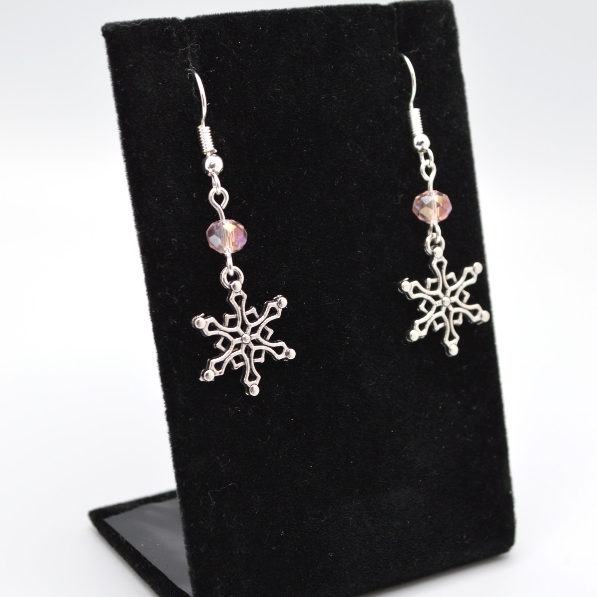 Silver snowflake earrings with pink beads on a black stand.